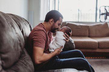 Bearded father bonding with newborn baby wrapped in white blanket