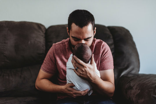 Loving father on leather couch holding swaddled newborn