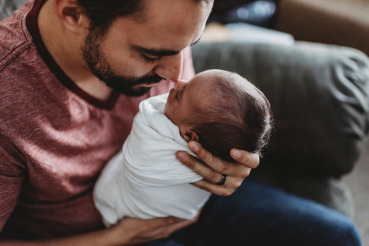 Mid-30?s dad with beard touching noses with swaddled newborn