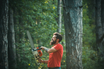 Lumberjack in the woods with chainsaw axe. Firewood as a renewable energy source. Stylish young man...