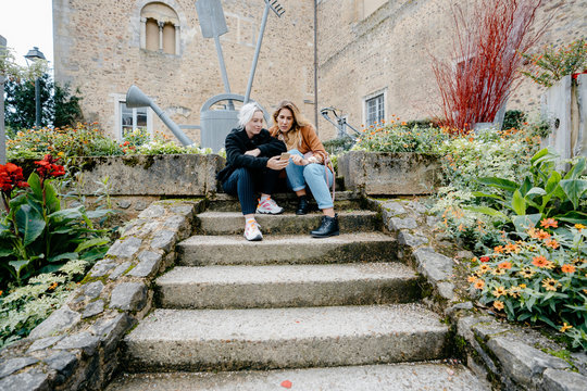 Young women using their smartphone sitted on stairs in a french town