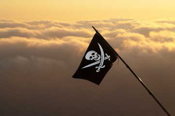 Jolly Roger (pirate flag) on wind and sea in sunset cloudy sky