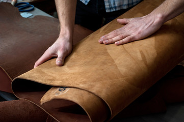 hands of a craftsman on leather rolls. chiaroscuro artistic, suede