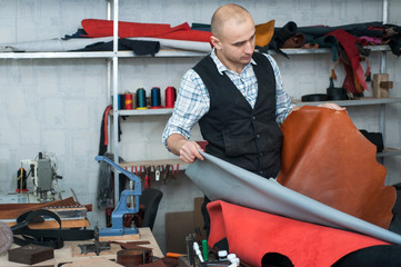 Fototapeta na wymiar craftsman in workshop, carefully examines the roll leather.