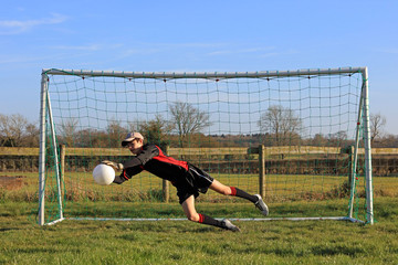 Young Goalkeeper Saving A Football In A Game Of Soccer.