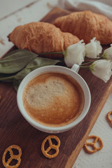 Romantic breakfast with a cup of coffee and croissants. Freshly brewed coffee with croissants and white flowers on a rustic vintage board.