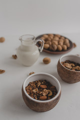 Obraz na płótnie Canvas A healthy breakfast of granola, oatmeal, cereals, nuts and milk. Cups with granola, a jug of milk, a plate with nuts on a white background.