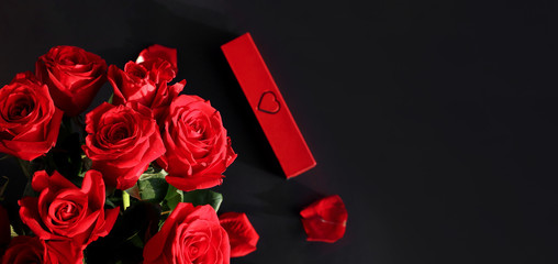 Beautiful bouquet of red roses and box with jewelry on a dark background