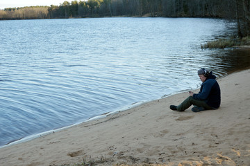 A man on headphones with a telephone near a forest lake.