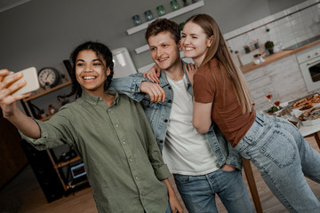 Obraz premium Let's take a selfie! A group of friends celebrate holidays at home and take a joint photo as a keepsake. International friendship, happy time together, friends having relax time. Enjoy communication
