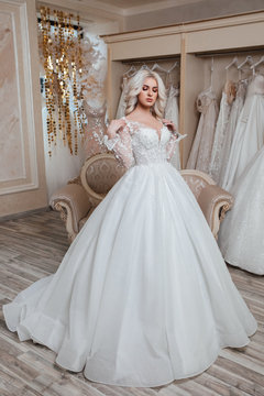 Fashion photo of beautiful woman with blond hair in luxurious wedding dress posing in modern wedding salon. Happy moment. Bride to be. Wedding makeup and hairstyle. 