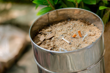 Many cigarette stub in sand ashtray. The rest of cigarettes in the ashtray. There are many types of cigarette stub on the sand in the ashtray. A cigarette is not good for health. 