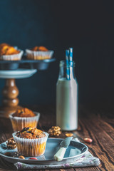Delicious cupcake with raisins, almonds and nuts. Homemade biscuit cakes. Vanilla caramel muffins in paper cups and bottles of milk on dark wooden background.