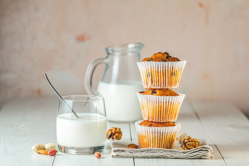 Vanilla caramel muffins in paper cups and bottles of milk on white wooden background. Delicious cupcake. Homemade biscuit cakes.