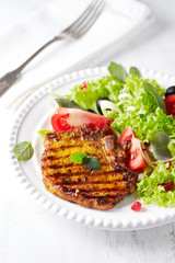 Grilled pork steak with fresh salad. White wooden background