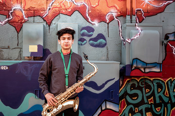 High school jazz band musician posing with saxophone by graffiti