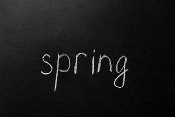 inscription "spring" written in white chalk on a black chalkboard.