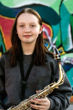 Female high school jazz musician posing with saxophone by graffiti