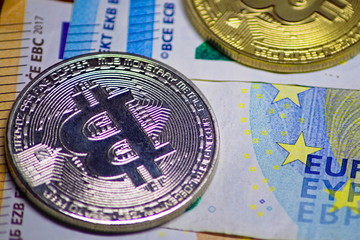 silver and gold bitcoin coin cryptocurrency with a ten and twenty euro banknotes as background