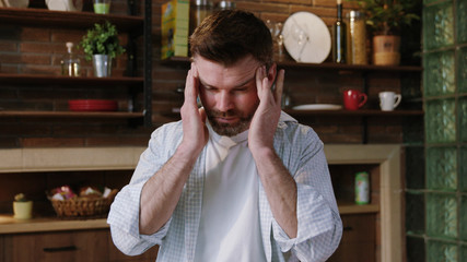 Portrait of a serious mature man sipping coffee from a cup holding a newspaper touching his hurting temples suffering from a bad headache.