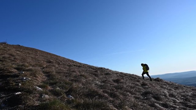 Wide locked down shot of a female hiking up the mountain slope in sunshine