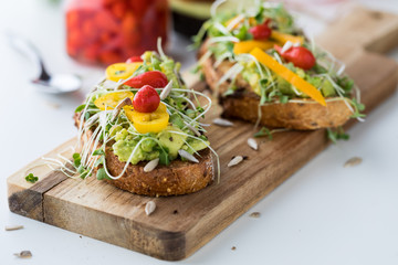 Close up of two avocado toasts topped with Peruvian drop peppers with a jar of the peppers in behind.