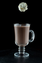 Hot chocolate with a scoop of vanilla ice cream, thrown into a glass on black background