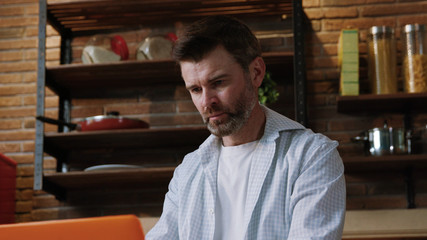 Successful serious enterpreneur working by the computer laptop sitting in the kitchen in his luxurious home apartment.