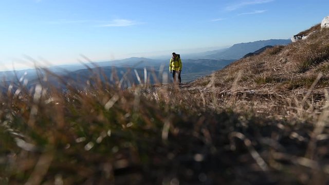 Wide low angle locked down shot of a female hiker walking up the mountain path in sunshine