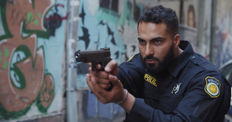 Police on duty. Portrait of severe bearded police officer holding aiming handgun looking forward....