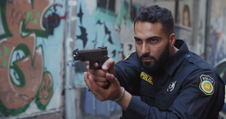 Police on duty. Portrait of severe bearded police officer holding aiming handgun looking forward. Crime scenein the city center.