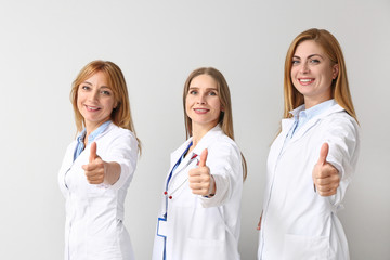 Fototapeta premium Portrait of female doctors showing thumb-up gesture on light background