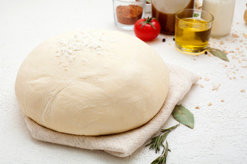 Dough on a white background, sprinkled with flour, decorated with spices, black pepper peas, olive oil, Bay leaf and mushrooms. Concept ingredients for baking or making dough.