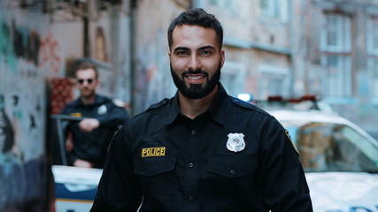 Strong smiling young man cops stand near patrol car look at camera enforcement officer police uniform auto safety security communication control policeman close up slow motion © Fractal Pictures