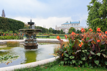 Fototapeta premium Vienna, Austria - September 1, 2019: Fountain in the Volksgarten (People's Garden) in Vienna with a view on the state Theater Burgtheater, Austria