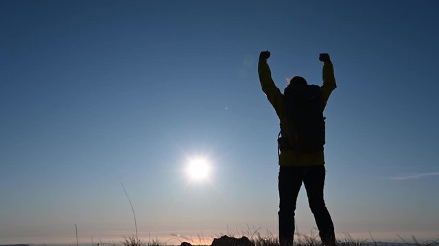 Low angle shot of the silhouette of a female hiking raising hands in victory when reaching the mountain top