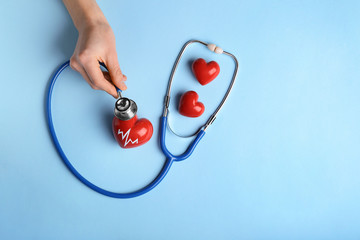 Female hand with red hearts and stethoscope on color background. Cardiology concept