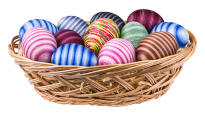 Colorful stripy ornate Easter eggs isolated on white background in wicker basket. Close-up of decorated eggshells. Handmade holiday decorations wrapped in thin cotton yarn glued to hollow egg shells.
