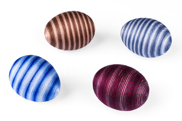 Four decorative streaked Easter eggs on white background. Close-up of blue, red or brown colored egg shells decorated with glued cotton sewing thread. Original holiday decoration from empty eggshells.