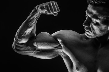 Strong Athletic Sexy Muscular Man on Black Background showing biceps. Black and White color tone.