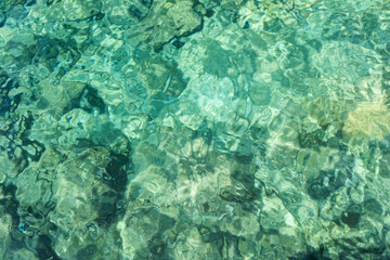 Obraz premium Rippled clear water in light green and turquoise colors and rocky ocean floor, viewed from above. Abstract natural full frame image.