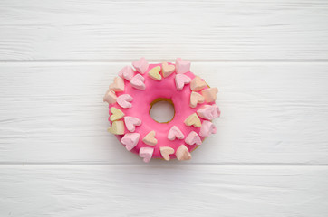 Sweet donut with pink frosting and decorative hearts on a white wooden colored background, top view...
