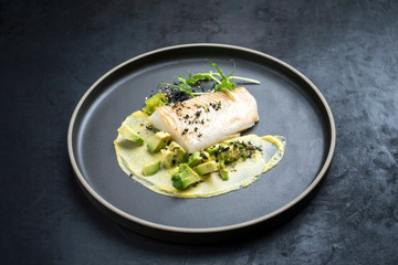 Gourmet fried cod fish filet with caviar, avocado slices and mustard mango creme as closeup on a...
