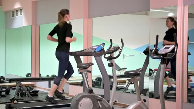 Beautiful woman running on a treadmill at gym. Fitness and healthy lifestyle concept. Sportswoman using run machine in fitness center.
