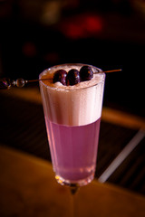 A purple Sauer cocktail in a tall glass with foam stands on the bar