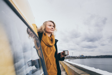 Young blond woman looking out of camper van overlooking the sea