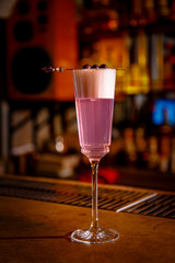 A purple Sauer cocktail in a tall glass with foam stands on the bar