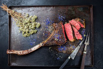 Gegrilltes dry aged Wagyu Tomahawk Steak mit Kräuter als Draufsicht auf einem schwarzen rustikalen...