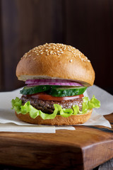 Closeup of home made beef burgers with lettuce served on little wooden cutting board. Dark background