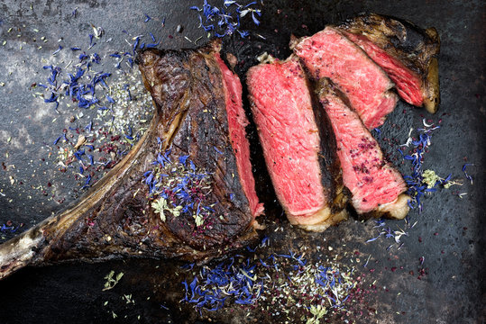 Barbecue dry aged wagyu tomahawk steak with herbs as top view on black rustic board
